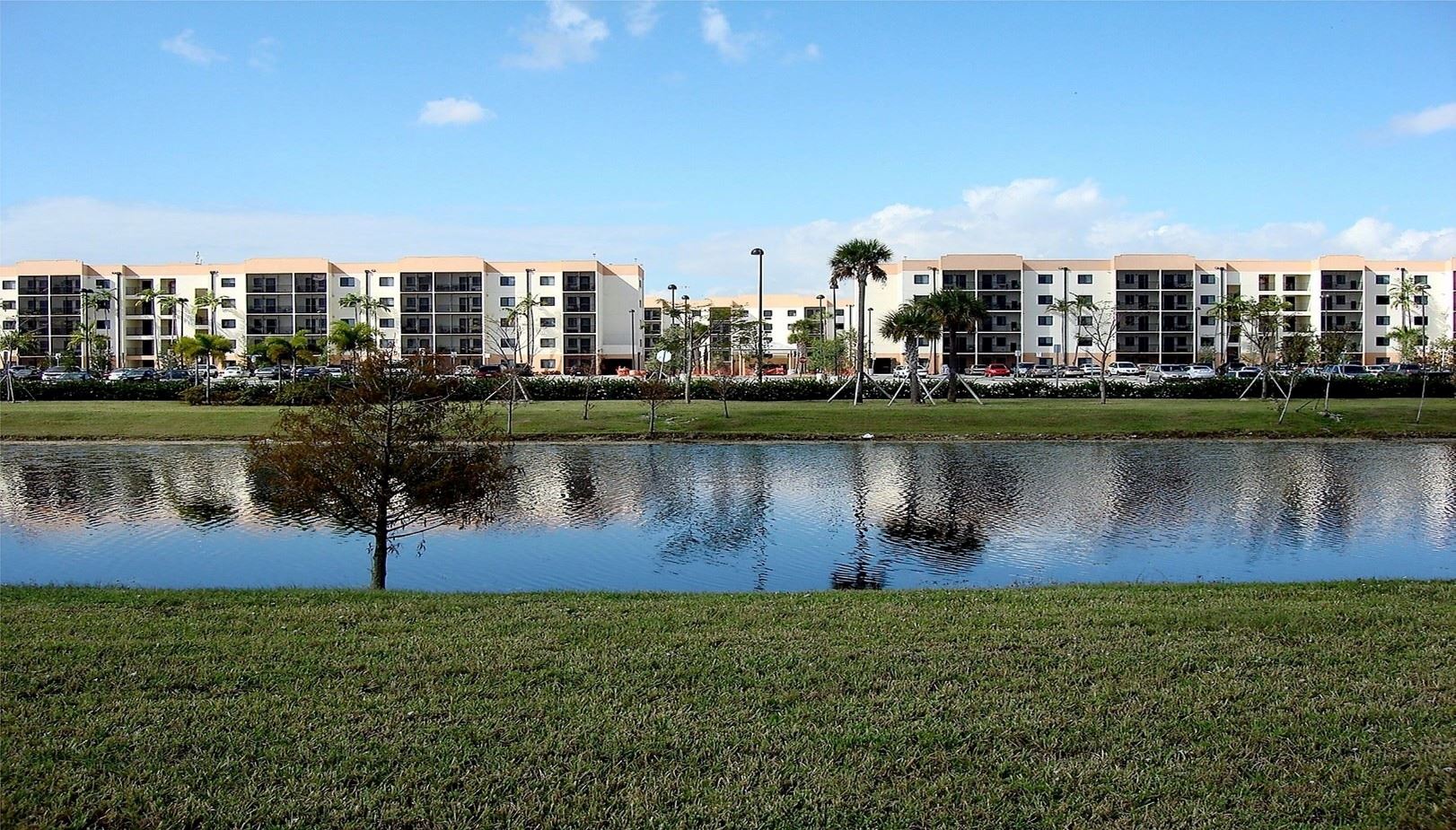 View from the lake within the Pines Place property, showing all three buildings of the complex along with the surrounding landscape.